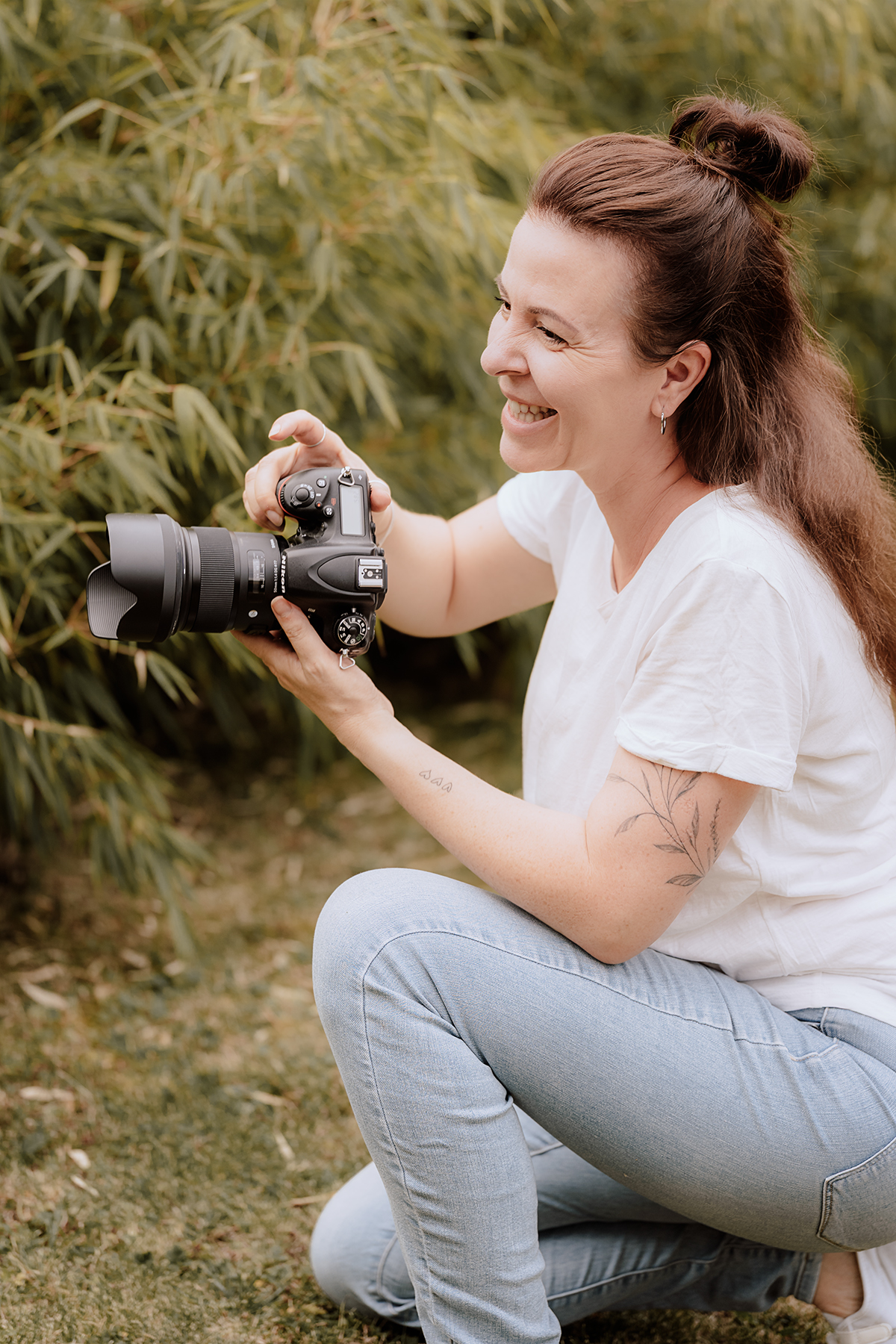 katja-jacobs-fotografin-im-einsatz Katja Jacobs kniet lachend im Garten und fotografiert mit der Kamera
