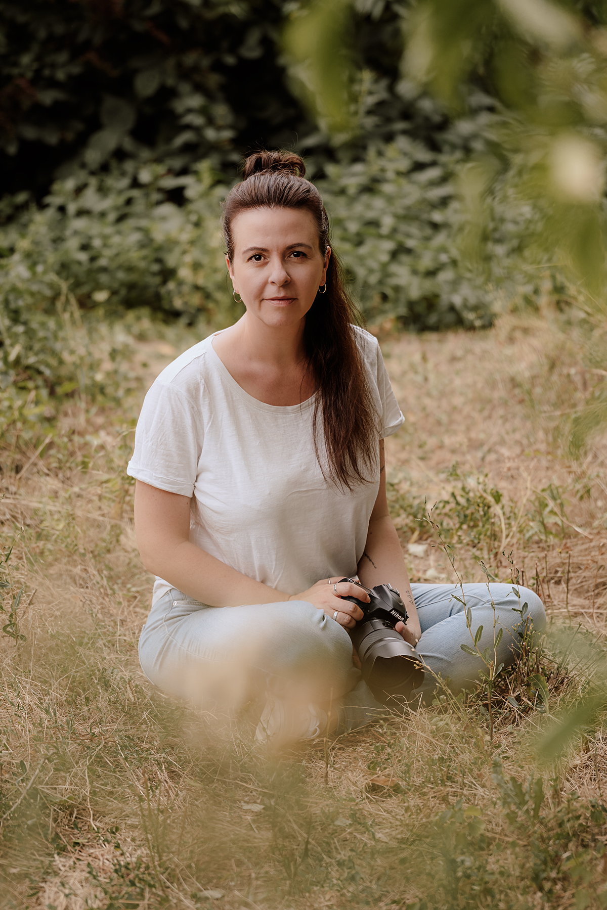 katja-jacobs-fotografin-mit-kamera-wiese Katja Jacobs sitzt mit Kamera im Schoß im Gras und blickt in die Kamera